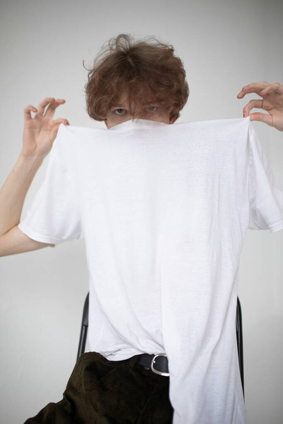 Attractive young european man isolated on light grey taking off his white shirt - Φωτογραφία, εικόνα