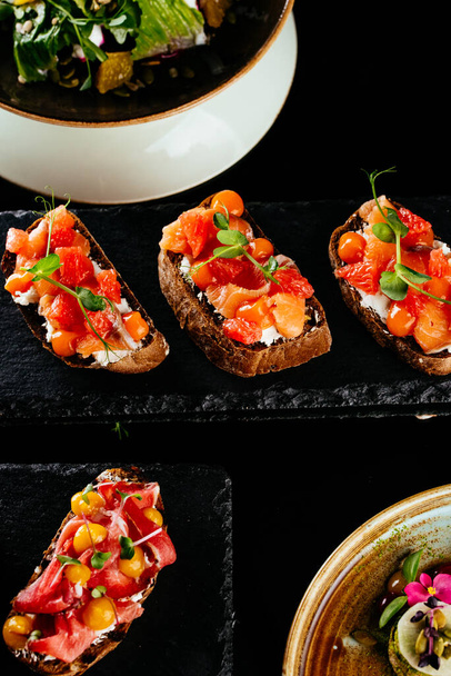 bruschetta con salmón, tomate y albahaca sobre fondo de piedra negra. - Foto, Imagen