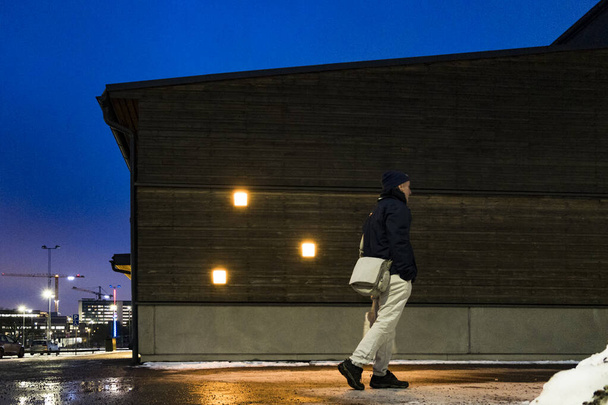 スウェーデンのストックホルムライトアップされた建物の隣の駐車場で夜歩く男. - 写真・画像