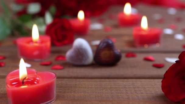 Sevgililer Günü konsepti çikolatalı şekerler kalp şeklinde ve ahşap üzerinde mumlar olan kırmızı güller. Aşk ve aşk kavramı. Dolly 4K çekti. - Video, Çekim