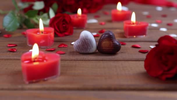 Sevgililer Günü konsepti çikolatalı şekerler kalp şeklinde ve ahşap üzerinde mumlar olan kırmızı güller. Aşk ve aşk kavramı. Dolly 4K çekti. - Video, Çekim