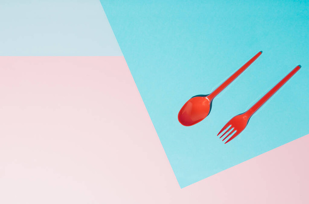 Red plastic fork and spoon against background in three color. Minimal concept - Zdjęcie, obraz