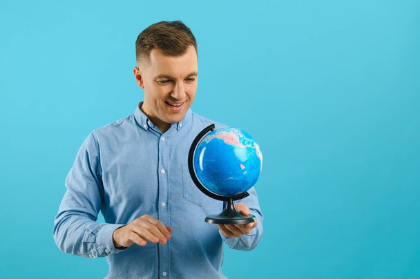 Excited traveler tourist man isolated on blue background. Passenger traveling abroad on weekends. Air flight journey concept. Holding world globe. - Фото, зображення