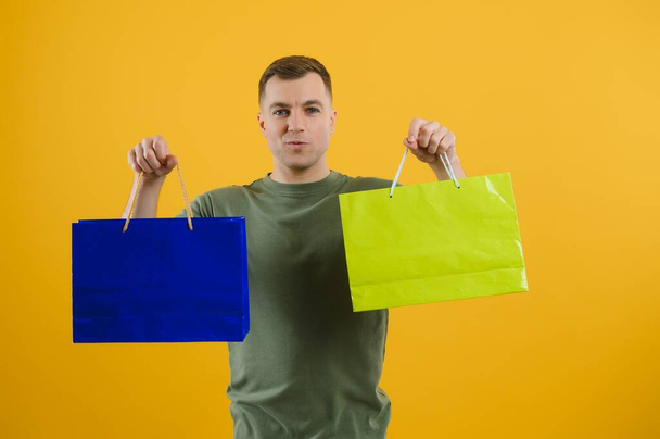 Portrait of young man with paper bags on yellow background. Space for text - Fotoğraf, Görsel