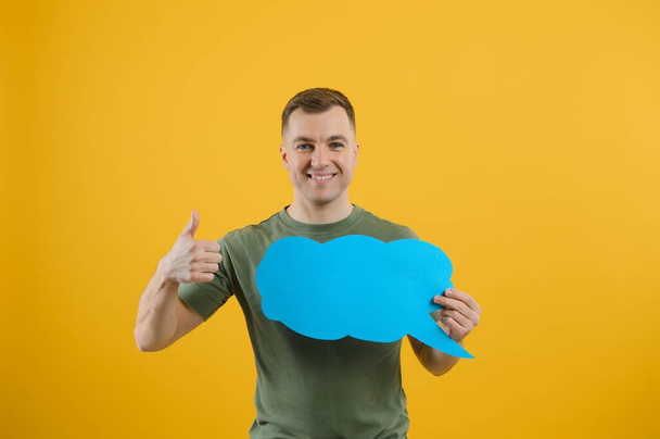 Young caucasian man isolated on yellow background holding a thinking speech bubble and doing OK sign - 写真・画像