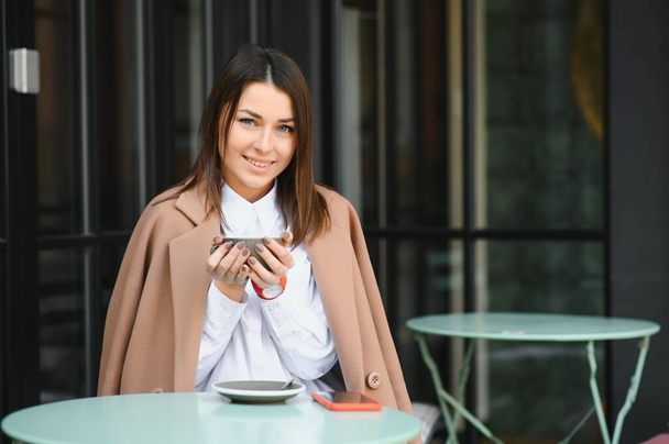 Portrait of young beautiful woman sitting in a cafe outdoor drinking coffee - Фото, изображение
