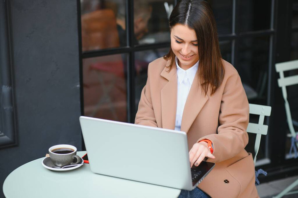 Фотопортрет чудової привабливої жінки, що працює на ноутбуці, сидячи в кафе, п'є каву
 - Фото, зображення