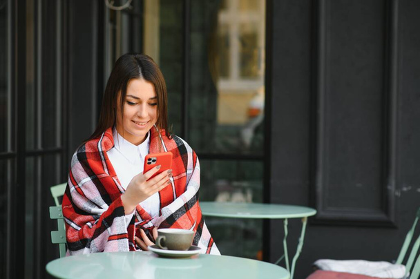 Portrait of young beautiful woman sitting in a cafe outdoor drinking coffee - Fotó, kép