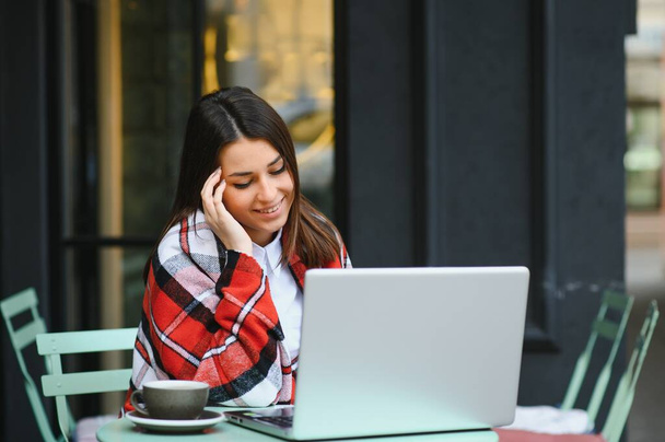 Young, a girl in an outdoor cafe with a laptop talking through a video call with someone, Aipi telephony - Foto, imagen