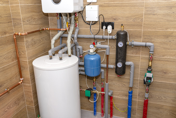 A modern gas boiler for natural gas, installed in a boiler room lined with ceramic tiles, 120 liter hot water tank visible. - Photo, Image