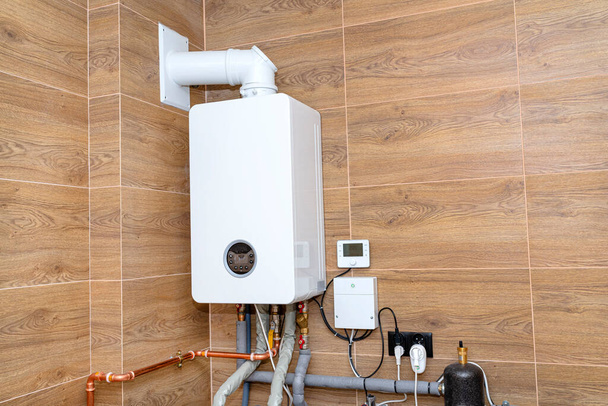 Ein moderner Gaskessel für Erdgas, installiert in einem mit Keramikfliesen ausgekleideten Heizraum. - Foto, Bild