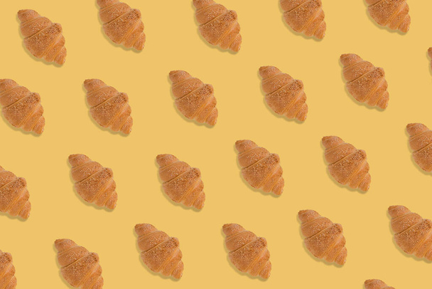 Creatief patroon gemaakt van vers gebakken croissant op felgele achtergrond. Minimaal concept van bakkerijproducten. - Foto, afbeelding