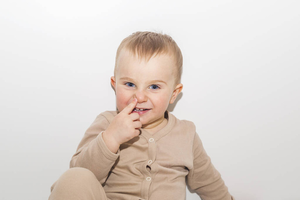 Kleine jongen wijst naar zijn neus op witte muur achtergrond - Foto, afbeelding