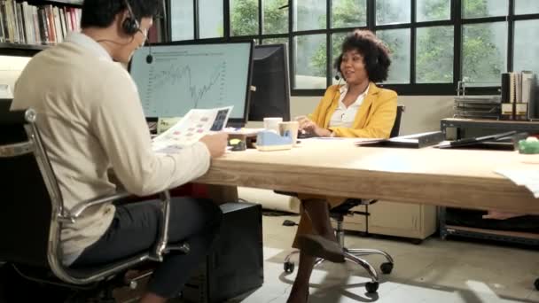 Két alkalmazott és munkatárs, afro-amerikai női és ázsiai férfi kollégák dolgoznak és beszélgetnek egy kommunikációs headsettel, hogy kapcsolatba lépjenek egy vállalkozással, ügyfélszolgálat a nyitott munkahelyi irodában. - Felvétel, videó