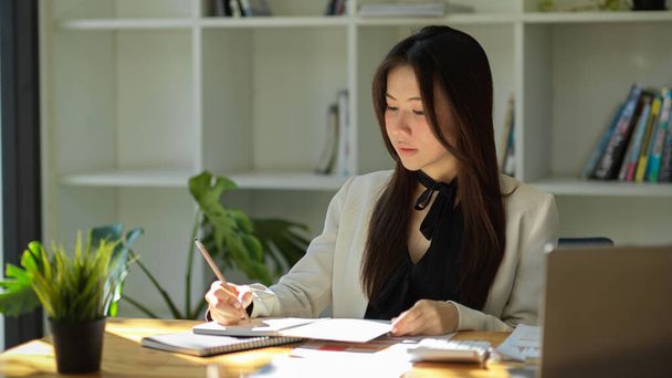 Atrakcyjna bizneswoman skupiająca się na pracy w biurze. Kobieta menadżer robi notatki na swoim notatniku. - Zdjęcie, obraz