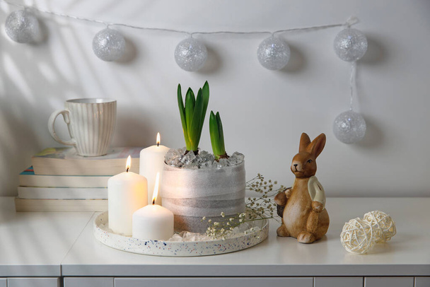 Unblown hyacinths with burning candles on a tray, a stack of books, a mug of tea, a garland of thread on the wall. Easter room decoration. - Foto, Imagen