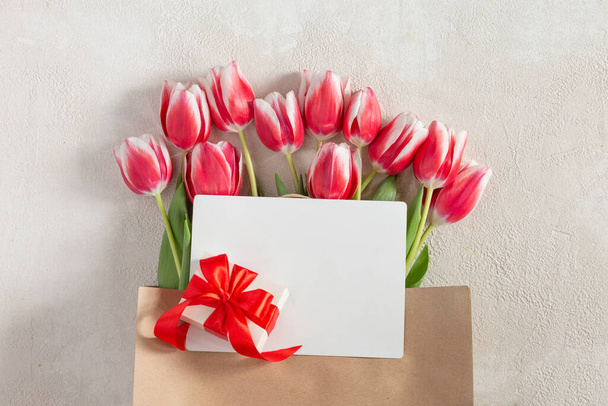 Den matek nebo Den žen, narozeniny, svatební gratulace. Jarní tulipány s dárkovou krabičkou a lahví vína v papírovém sáčku. - Fotografie, Obrázek