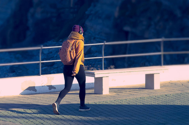 Meisje in een oranje jasje die onderweg naar muziek luistert - Foto, afbeelding