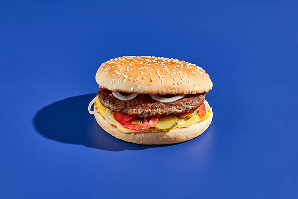 Beef burger blue background with hard shadow. American junk food minimal style. Hamburger trendy style.  Simple burger colour background - Photo, Image