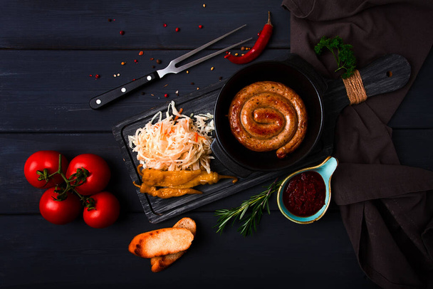 Piatto tradizionale tedesco, Salsiccia a spirale fritta, con crauti, con salsa rossa, su uno sfondo di legno grigio scuro, vista dall'alto, orizzontale, senza persone, - Foto, immagini