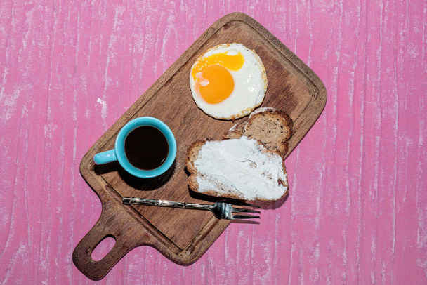 Tabakta kızarmış yumurta dilimi pembe arka planda izole edilmiş kesme tahtasının içinde espresso kahvesi var. Üst manzara, kahvaltı ve içecek konsepti.. - Fotoğraf, Görsel