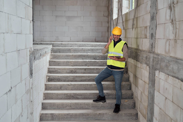 Kaukázusi mérnök áll a lépcsőn, és böngészés digitális tabletta az építési területen - Fotó, kép