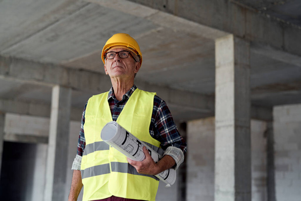 Ανώτερος καυκάσιος άνδρας που κρατά σχέδια στο εργοτάξιο  - Φωτογραφία, εικόνα