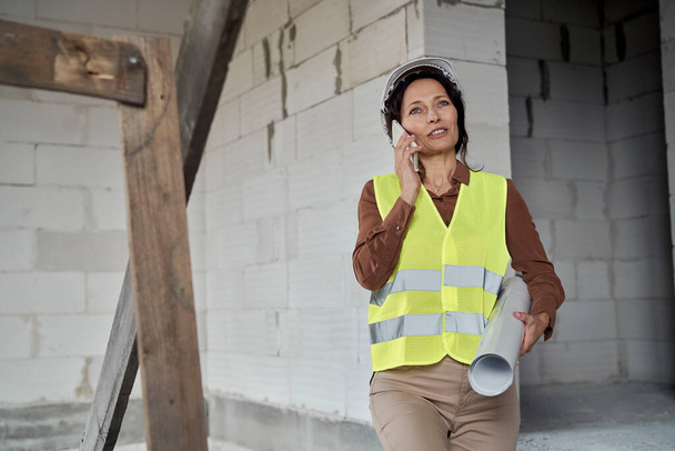 Nainen kypsä valkoihoinen insinööri liikkuu portaissa rakennustyömaalla ja puhuu yksi matkapuhelin  - Valokuva, kuva