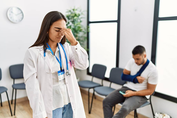 Young asian doctor woman at waiting room with a man with a broken arm tired rubbing nose and eyes feeling fatigue and headache. stress and frustration concept.  - Photo, Image