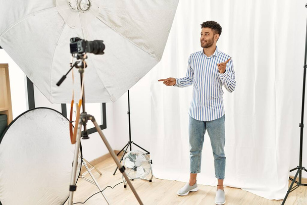 Arabský mladý muž vydávající se za modelku ve fotografickém studiu a usmívající se sebevědomě ukazující prsty do různých směrů. kopírovat místo pro inzerci  - Fotografie, Obrázek