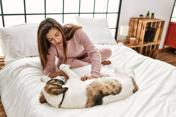 Young woman smiling confident playing with dog sitting on bed at bedroom - Photo, Image