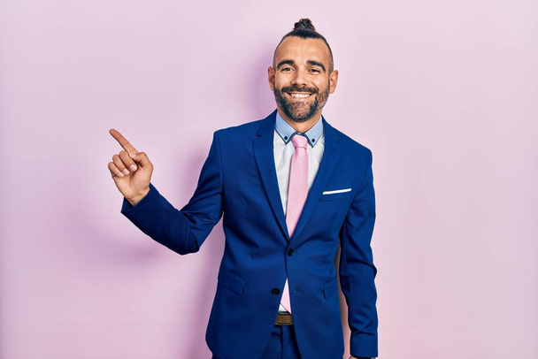 Young hispanic man wearing business suit and tie with a big smile on face, pointing with hand finger to the side looking at the camera.  - 写真・画像