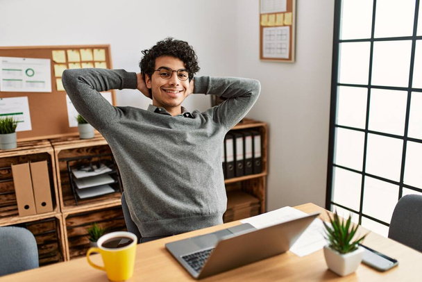 Jovem empresário hispânico relaxando com as mãos na cabeça no escritório. - Foto, Imagem