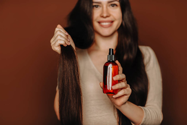 Uzun, sağlıklı kahverengi saçlarını tutan ve kamera şampuanı ya da saç kremi kullanan, doğal paraben ücretsiz saç bakım ürünleri kullanan bir kadının stüdyo portresi. - Fotoğraf, Görsel
