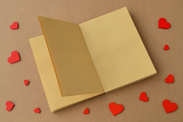 Open book or notebook made of kraft paper, red hearts on table. Valentines day, Valentine card, love - Fotoğraf, Görsel