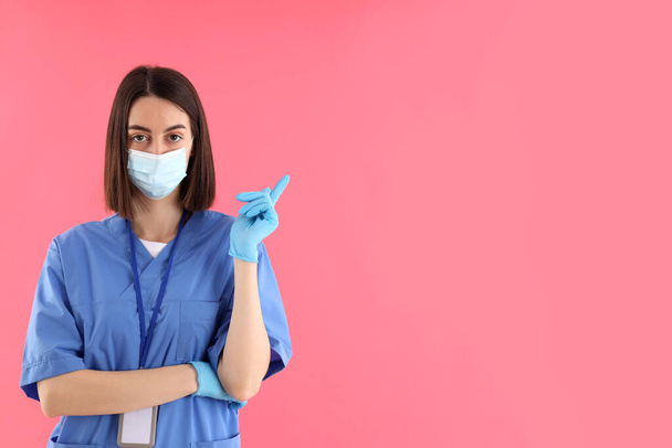 Γυναίκα εκπαιδευόμενη νοσοκόμα σε γάντια και μάσκα σε ροζ φόντο - Φωτογραφία, εικόνα