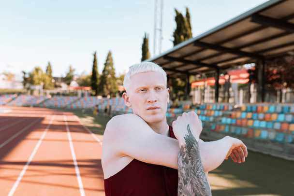Albino erkek atlet pist esneme hareketleri yapıyor, şampiyon. - Fotoğraf, Görsel