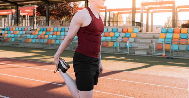 albino male athlete on running track stretching, bleachers in background, sunset - Foto, imagen