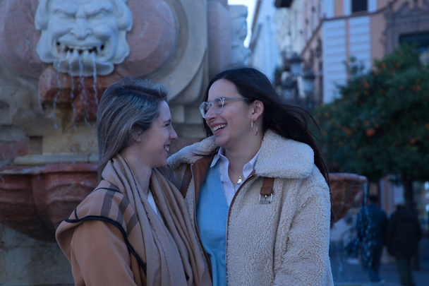 Настоящая пара молодых женщин, сидящих в фонтане, смеясь и разговаривая. Fellobiq +, лесбиянки, влюбленные, инклюзии. - Фото, изображение