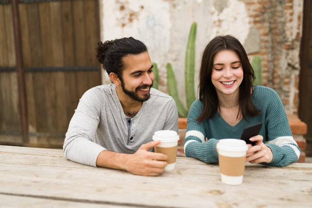 Fröhliche Freunde lachen und scherzen, während sie auf ihrem Smartphone die sozialen Medien betrachten. Paar entspannt sich und hängt in einem Café herum - Foto, Bild