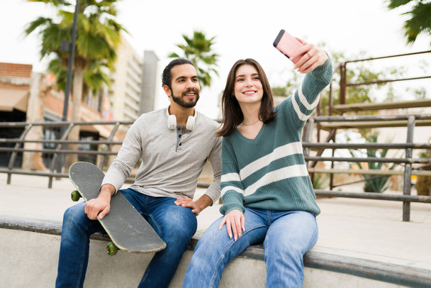 Běloška žena ve svých 20s přičemž selfie se svým nejlepším přítelem, zatímco dělá skateboarding v parku  - Fotografie, Obrázek