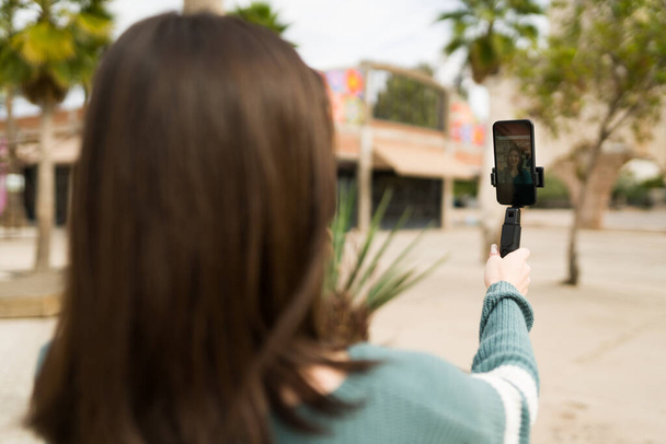 Gen z influencer vidět zezadu drží smartphone s stativem a natáčí se pro video vlog na sociálních sítích  - Fotografie, Obrázek