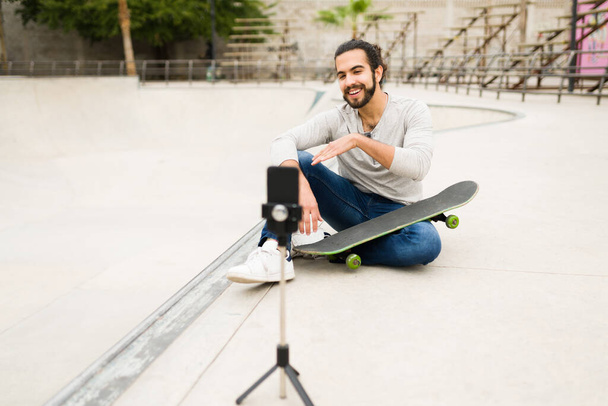 Atrakcyjny social media influencer rozmawiający z kamerą podczas nagrywania video vlog w skateboardowym parku  - Zdjęcie, obraz