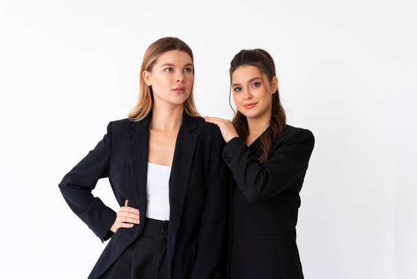 Concept of partnership in business. Two Young businesswoman dressed black formal suit standing studio isolated white background. Brunette woman put her hands on the shoulders of her friend. - Foto, Imagem