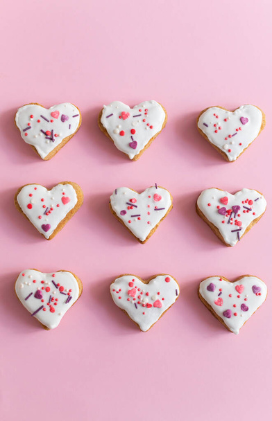 Gingerbread covered with white icing and sprinkling on a pink background. The concept of celebrating Valentine's Day. Vertical orientation. Top view. - Photo, Image