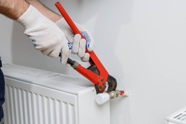Turuncu kasklı bir işçi eve radyatör yerleştirir. - Fotoğraf, Görsel