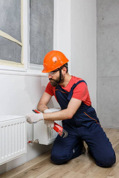 pracovník v oranžové helmě instaluje v domě radiátory - Fotografie, Obrázek