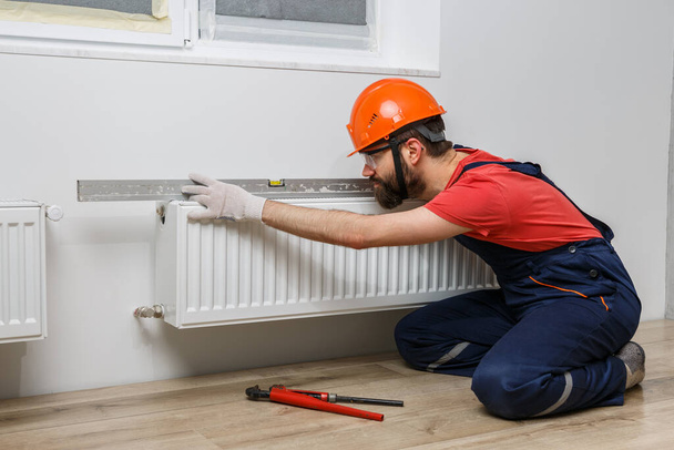 a worker in an orange helmet installs radiators in the house - Photo, Image