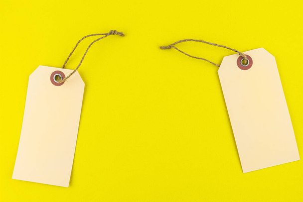 Δύο λευκές καφέ ετικέτες δώρων με μια χορδή που βρίσκεται σε ένα κίτρινο φόντο από σφουγγάρι, στις πλευρές. - Φωτογραφία, εικόνα