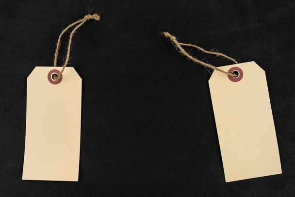 Dos etiquetas de regalo marrón en blanco con una cuerda acostada sobre un fondo negro hecho de esponja, en los lados. - Foto, imagen